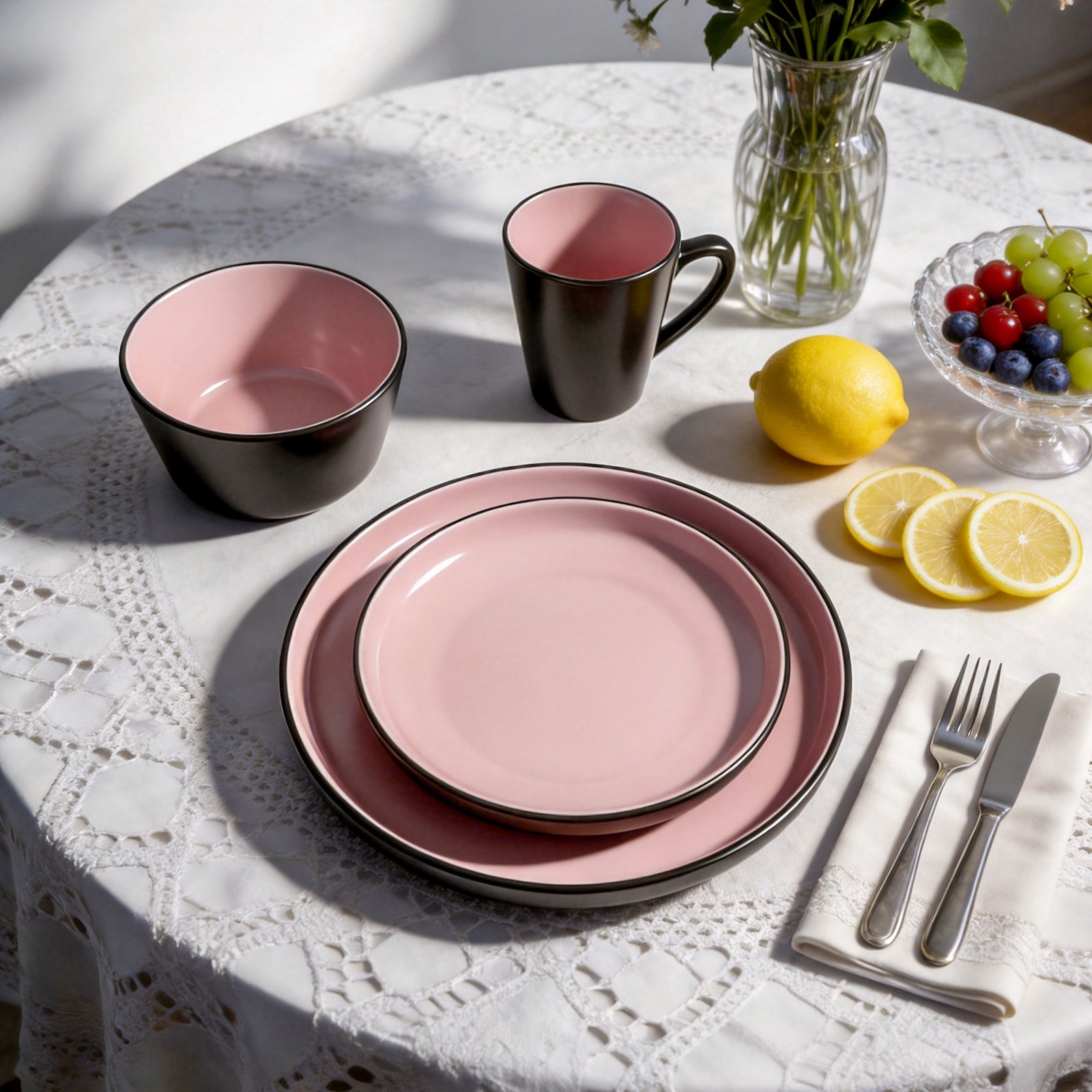 Pink ceramic tableware set on a white lace tablecloth with lemons and grapes.