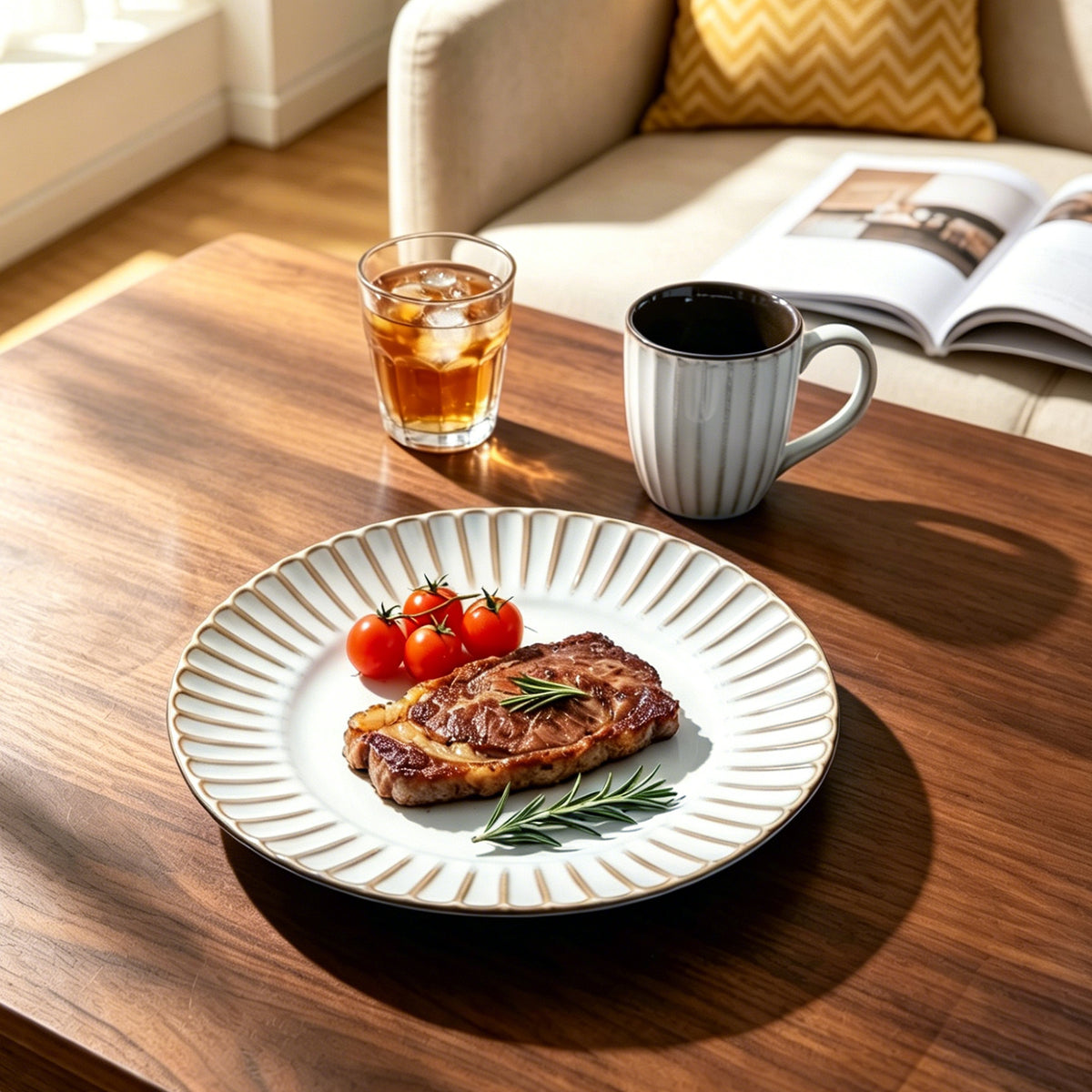 A round white ceramic plate with a fluted rim and subtle vertical ridges, styled with a cooked steak, cherry tomatoes, and rosemary on a wooden table. A striped mug, an iced drink, and an open magazine are visible in a cozy indoor setting.