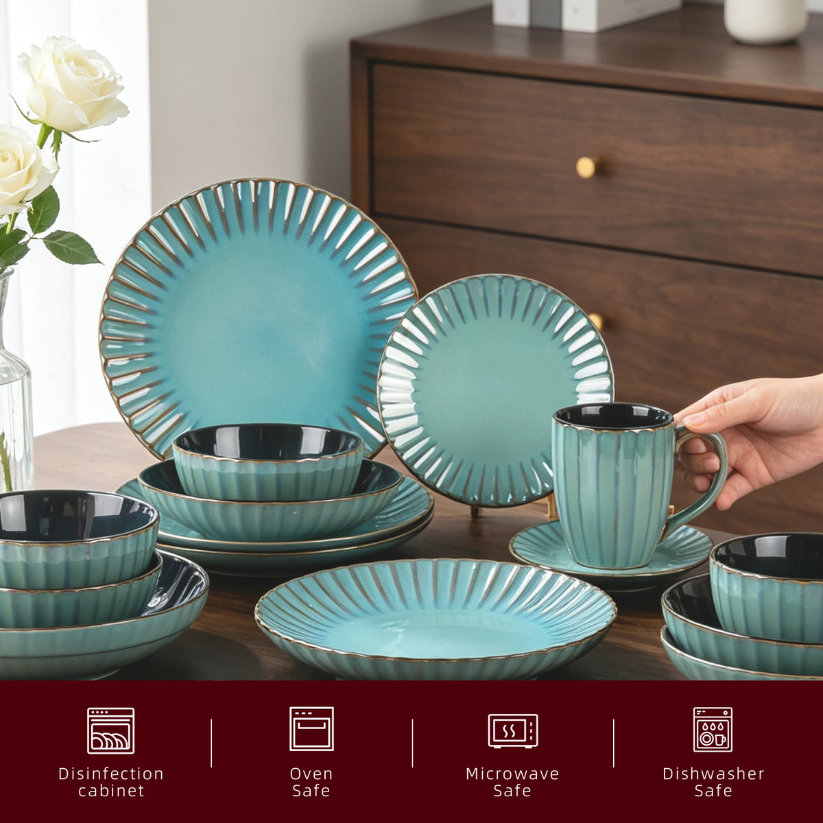 A coordinated ceramic dinnerware set in a light aqua/turquoise ribbed glaze with dark interior rims and metallic gold-toned edges, displayed on a wooden table. A hand is holding one of the cups, and a vase of white roses and a wooden cabinet are visible in the background.