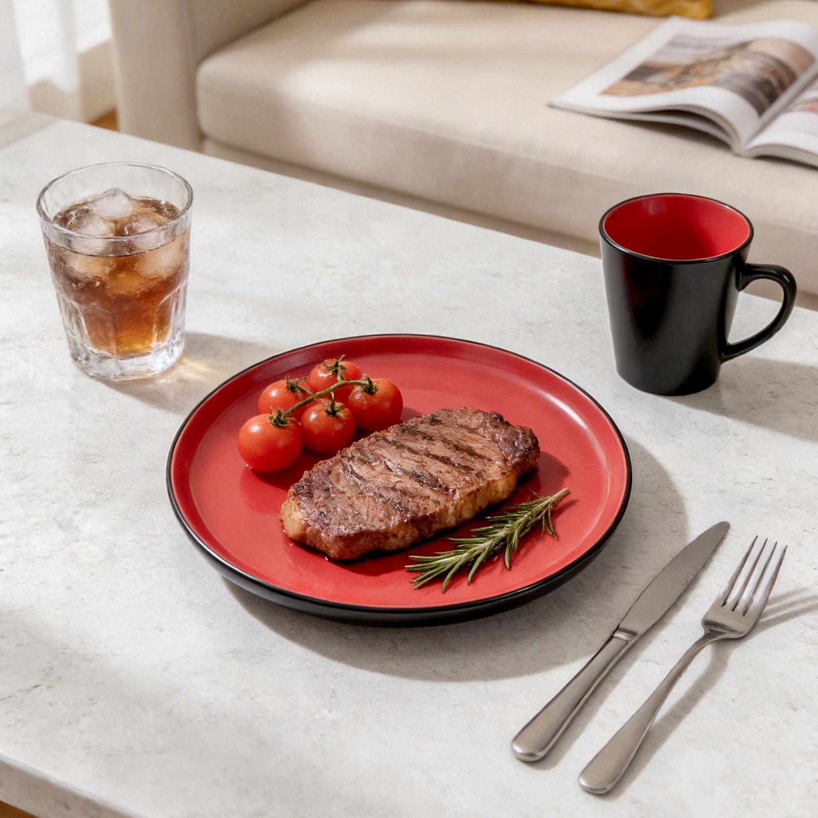 Steak on a red plate with tomatoes and a black mug on a table.