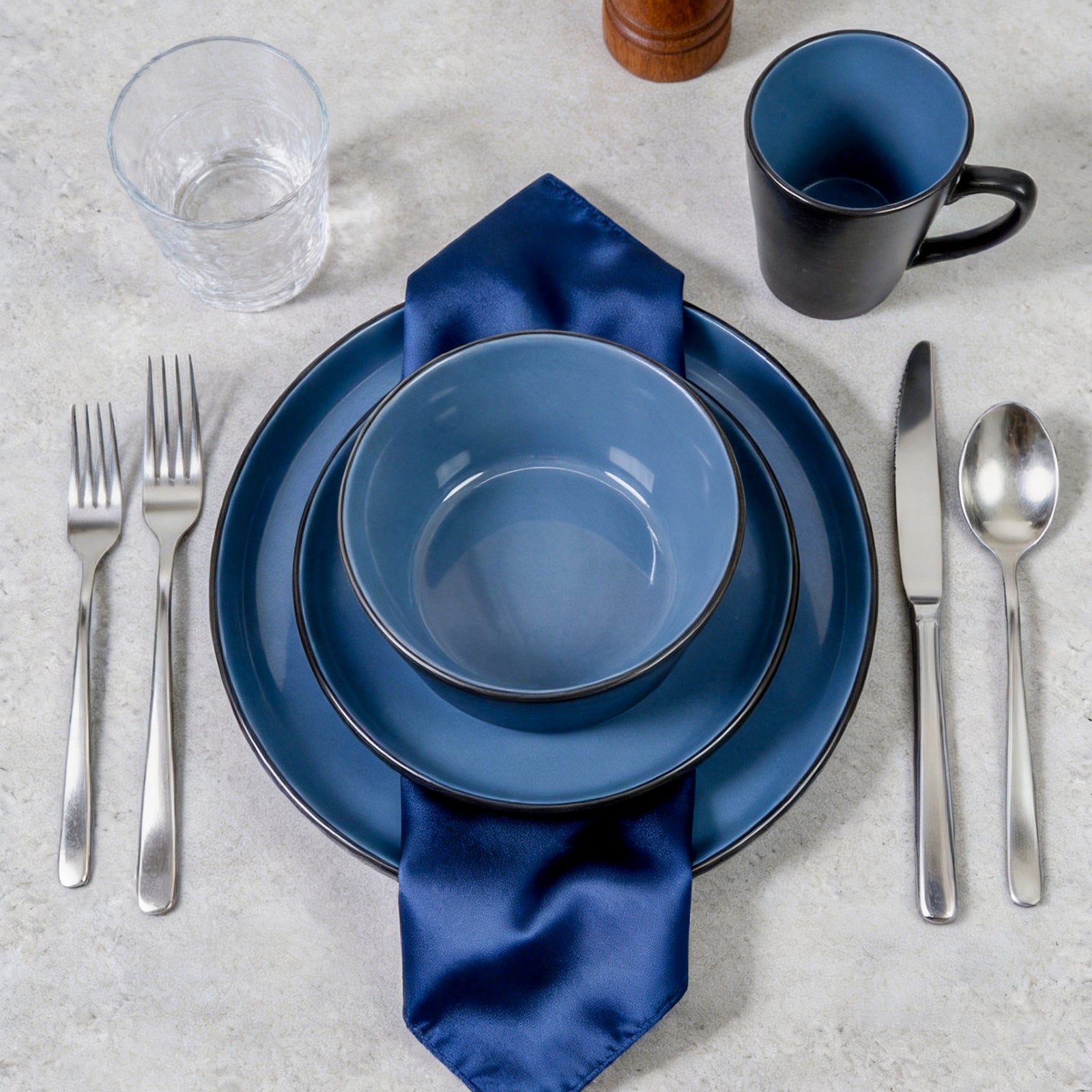 Blue ceramic tableware set with silver cutlery on a light gray surface