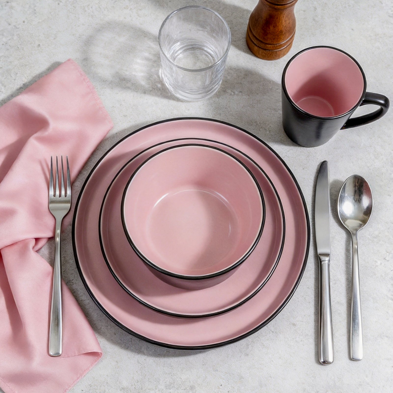 Pink ceramic plates with black rim, silverware, and a pink mug on a light gray surface.