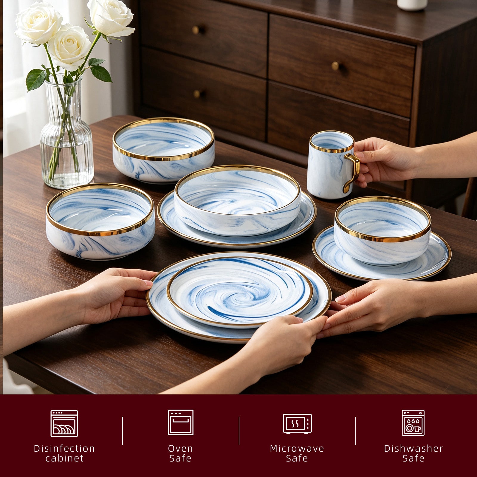 A set of ceramic tableware including plates, bowls, and a mug with a blue marble pattern and gold trim, arranged on a dark wooden table with hands holding some pieces. A vase of white roses is on the left, and a dark wood cabinet is in the background.