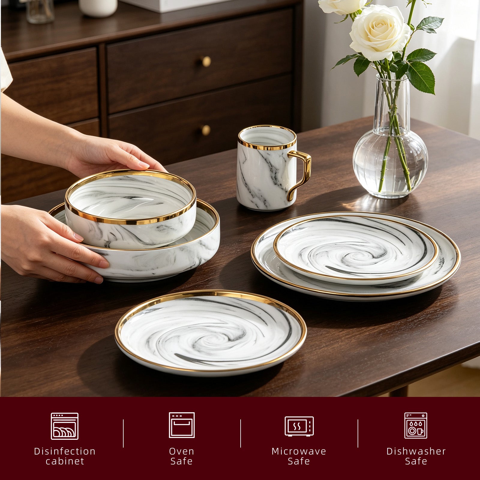 A set of white and gray marble-patterned dinnerware with gold trim, including plates, bowls, and a matching mug, arranged on a dark wooden table. A person's hands are visible holding a stack of bowls on the left, and a glass vase with white roses sits in the background.