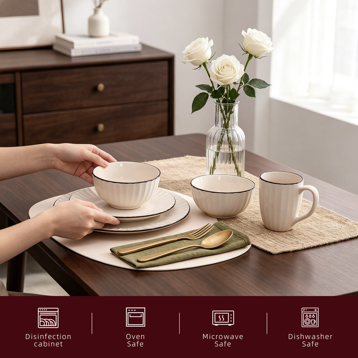Cream-colored ceramic tableware set with a thin dark rim, shown on a wooden dining table with hands placing a bowl. A glass vase with white roses, a woven placemat, gold-toned cutlery, and a matching mug are also visible.