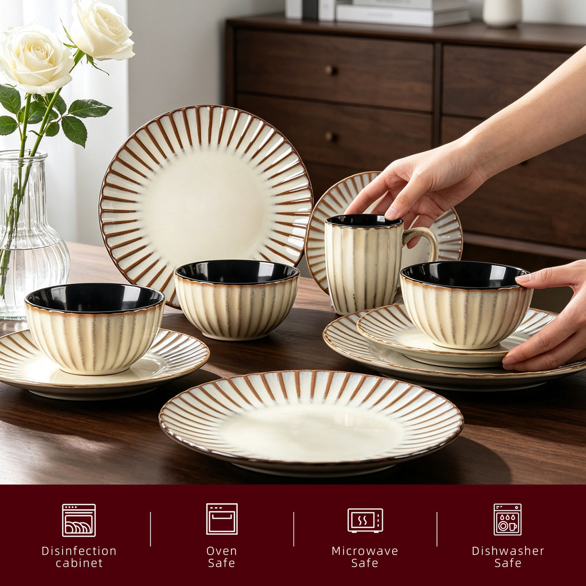 A set of beige ceramic tableware with brown radial stripes and black interiors, shown on a wooden table with hands holding some pieces. White roses in a vase and a dark wood cabinet are in the background.